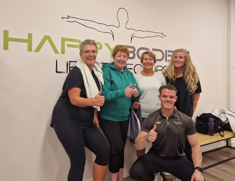 Leden van Happy Bodies met hun trainer voor het logo in de club